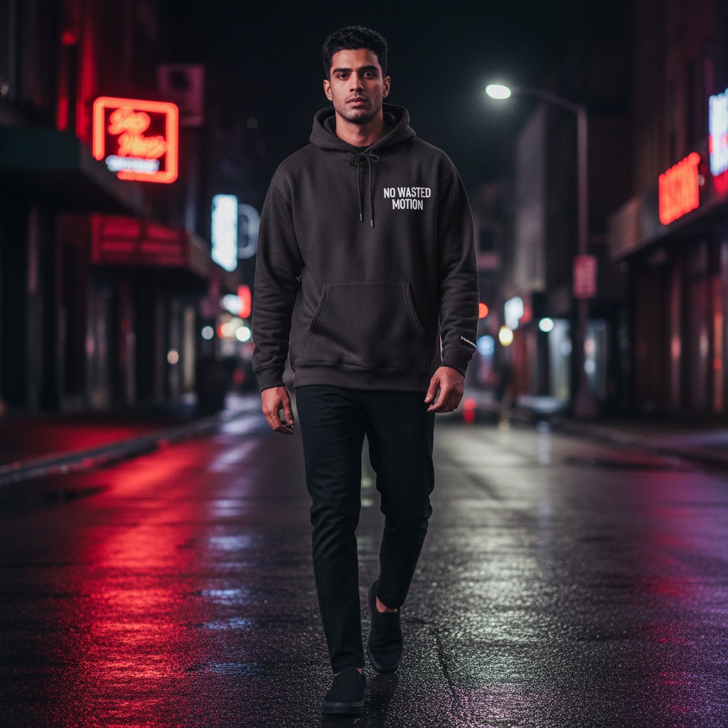 TunedForm Society heavyweight black hoodie with white text on a man walking on a wet city street at night