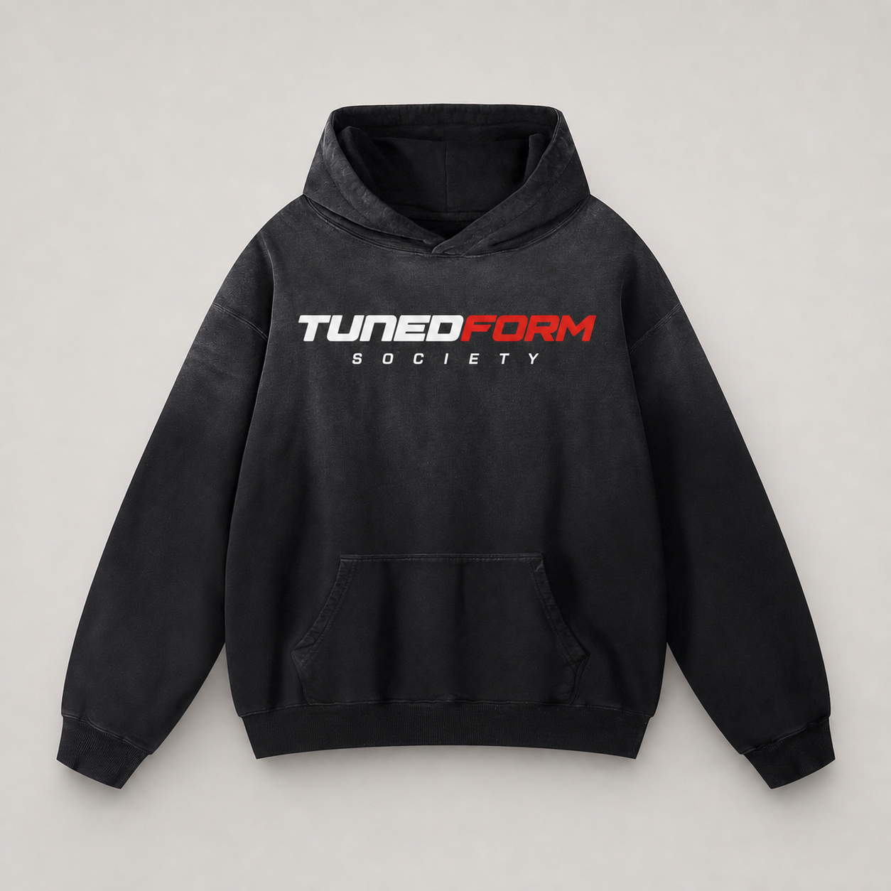 Front view of the black TunedForm Society sunfade heavyweight oversized hoodie on a warm gray studio background