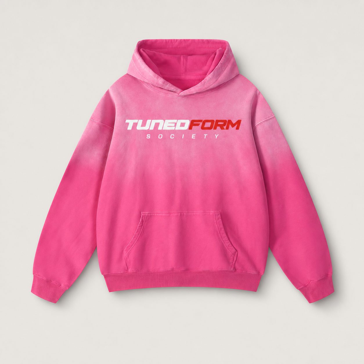 Front view of the pink TunedForm Society sunfade heavyweight oversized hoodie on a warm gray studio background